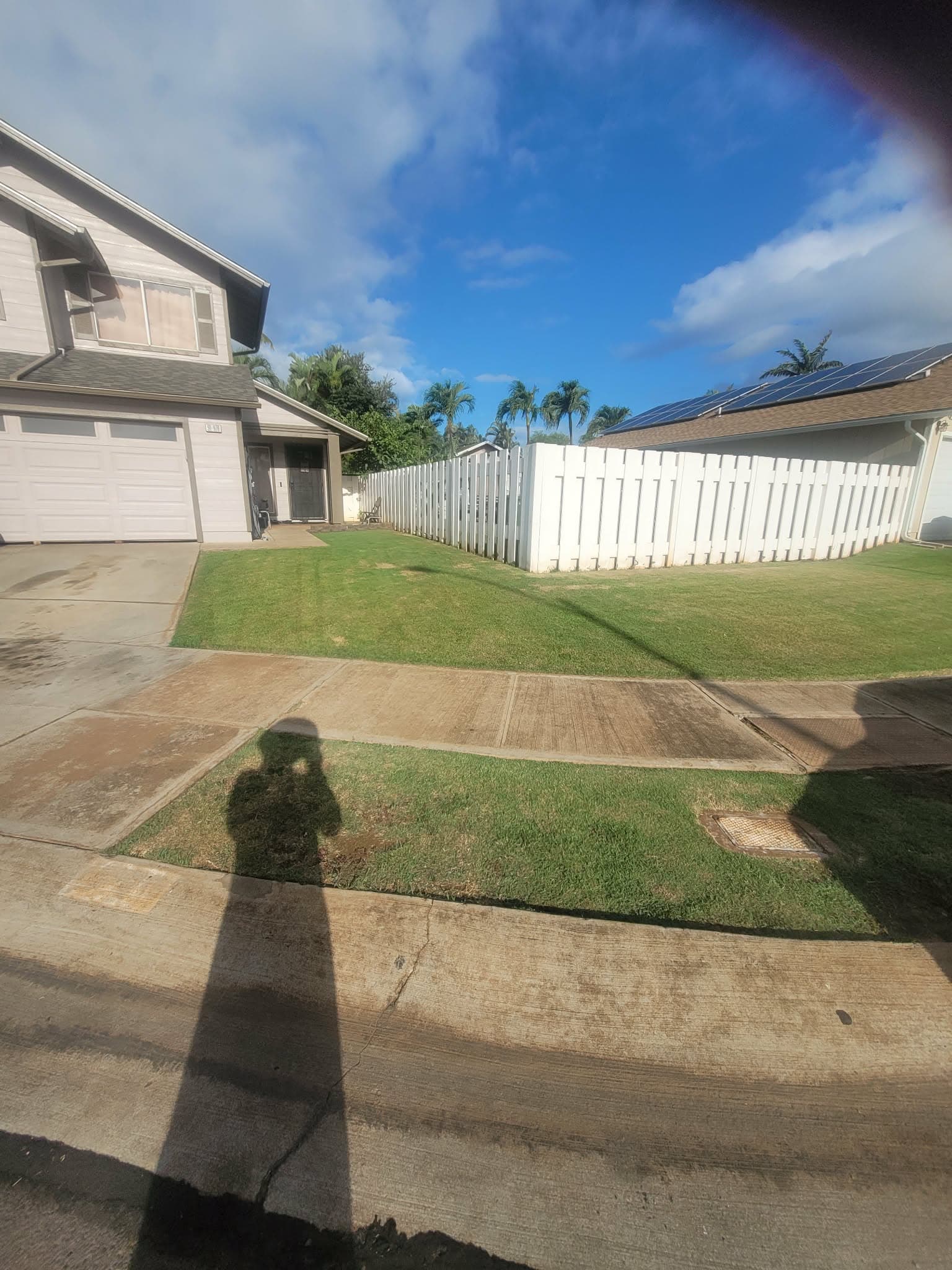 Side yard mowed along a white fence in an Oahu neighborhood